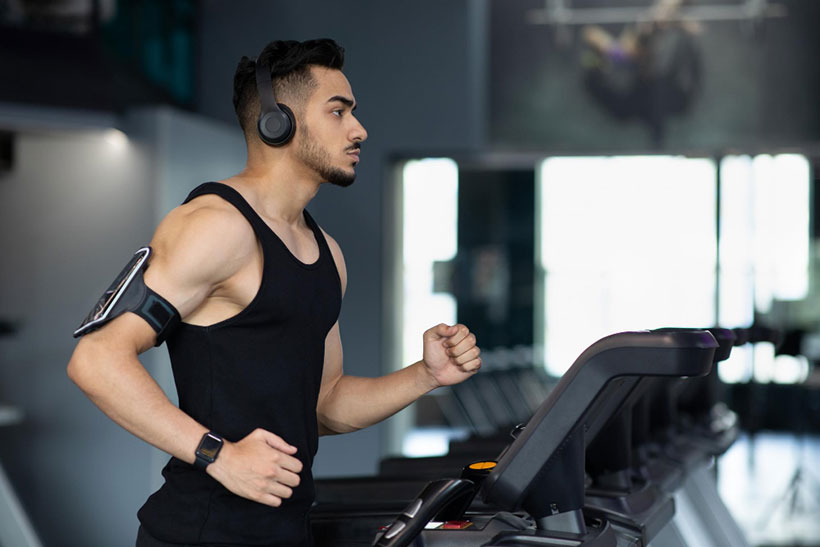 Athlete wearing wireless headphones and running on a treadmill in a gym