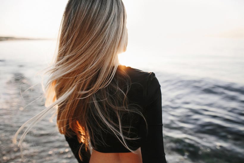 Une jeune femme sur la plage, ses longs cheveux blonds au vent